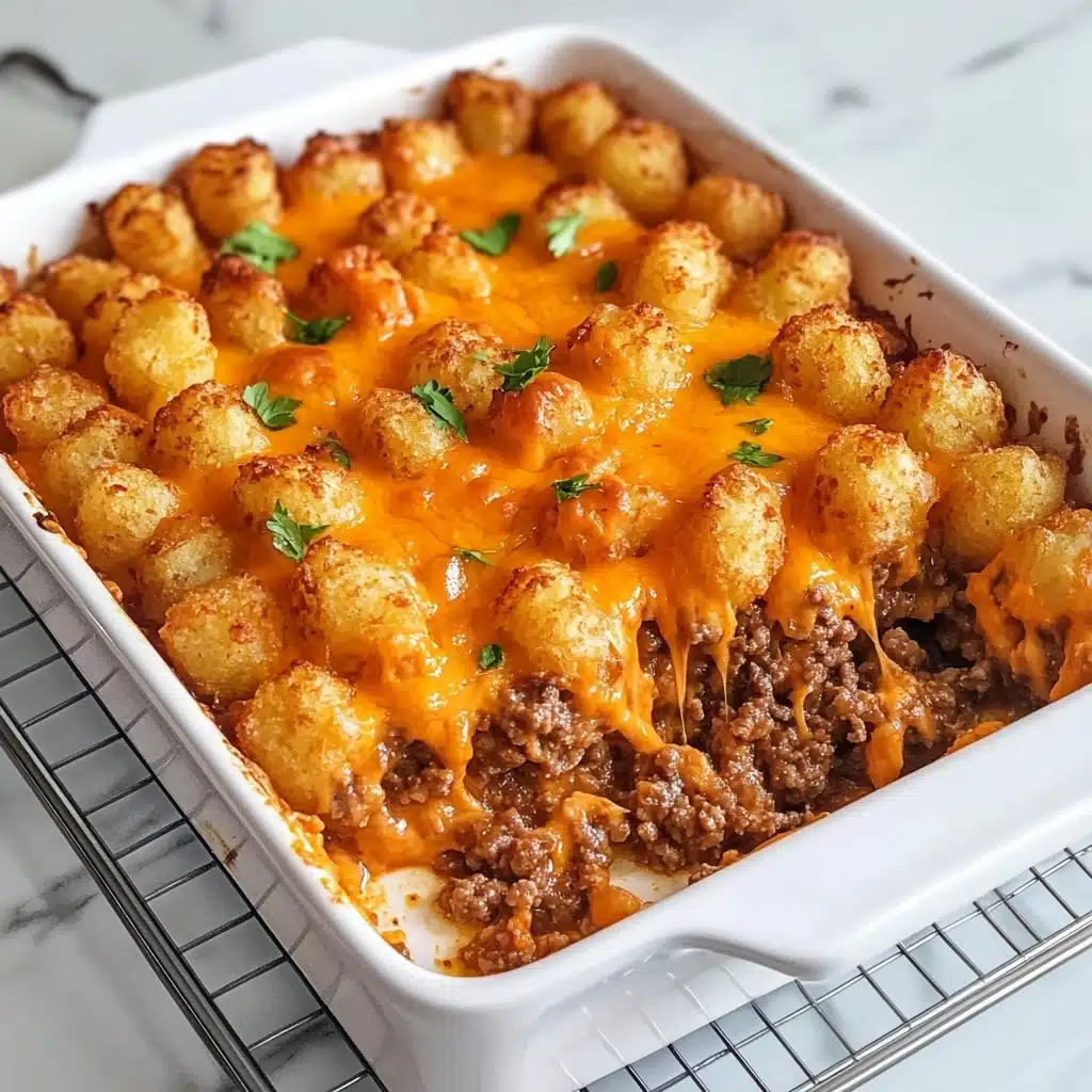 Tater Tot Casserole, easy tater tot casserole, comfort food recipes, hearty beef casserole, crispy tater tot bake The image shows a white rectangular baking dish filled with a dish that has two visible layers. The top layer is made of golden brown tater tots with a slightly crispy texture and melted orange cheese drizzled on top, garnished with small green herb pieces. The bottom layer consists of cooked ground beef with a crumbly texture and a rich brown color. Part of the dish has been scooped out, revealing the distinct layers. The baking dish is placed on a silver wire rack over a white marbled surface.
