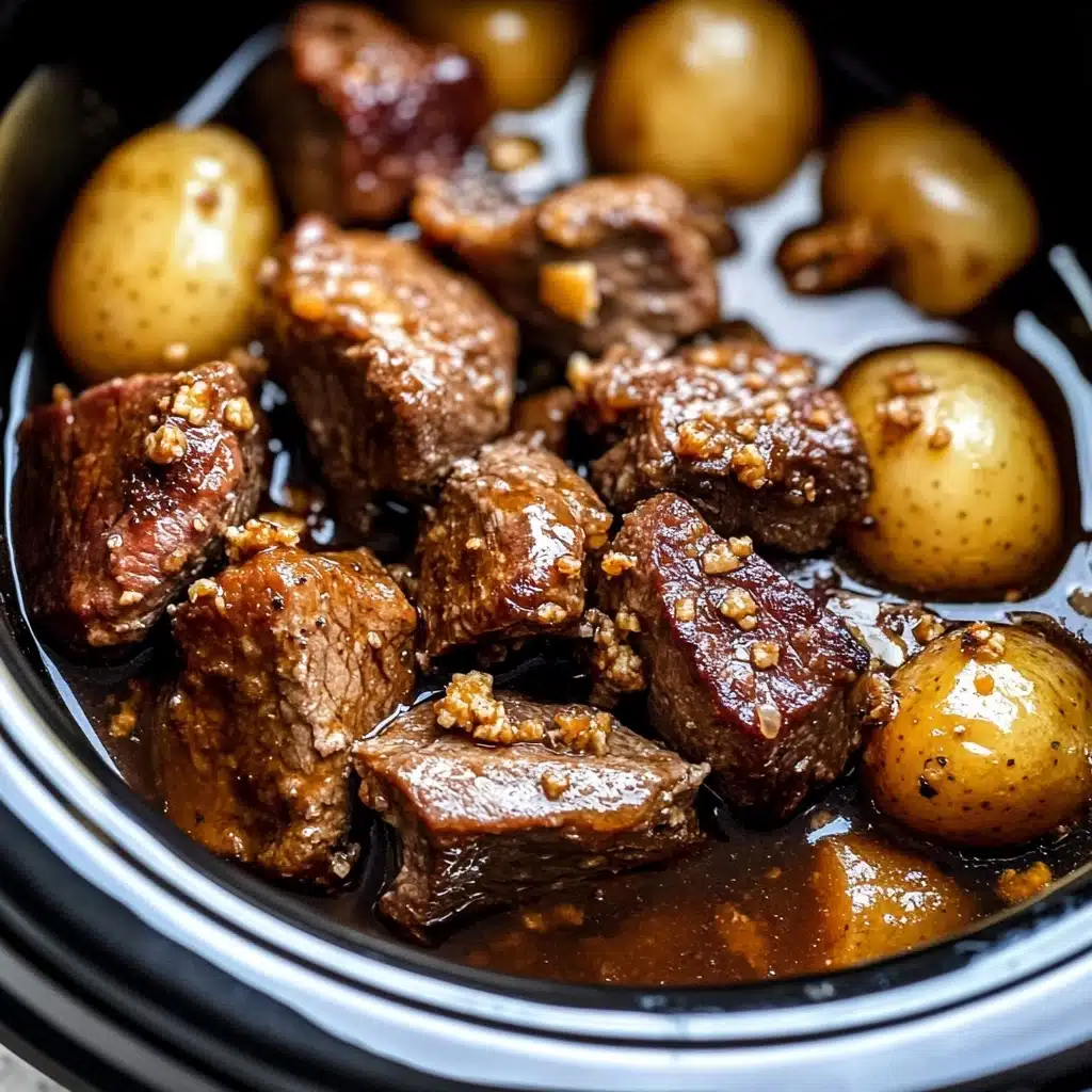 Slow Cooker Garlic Butter Beef Bites, beef stew in slow cooker, easy beef dinner recipes, hearty beef meals, comforting slow cooker recipes The image shows a close-up of chunks of cooked meat with a brown, slightly crispy outer layer mixed with small grains of seasoning, sitting in a rich, glossy brown sauce. Surrounding the meat are round, soft-looking whole potatoes with a light golden color. The food is inside a black slow cooker with a visible edge, and the background is a white marbled texture.