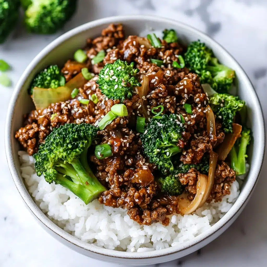 Ground Beef and Broccoli Stir Fry, easy ground beef stir fry, healthy broccoli stir fry, quick weeknight dinner, savory Asian beef stir fry A white bowl filled with a base layer of soft white rice, topped with a mix of dark brown cooked ground meat and bright green broccoli florets. Scattered light brown cooked onion pieces and small chopped green onions are mixed with the meat and broccoli. Tiny white sesame seeds are sprinkled on top, adding texture to the colorful dish, all placed on a white marbled surface.