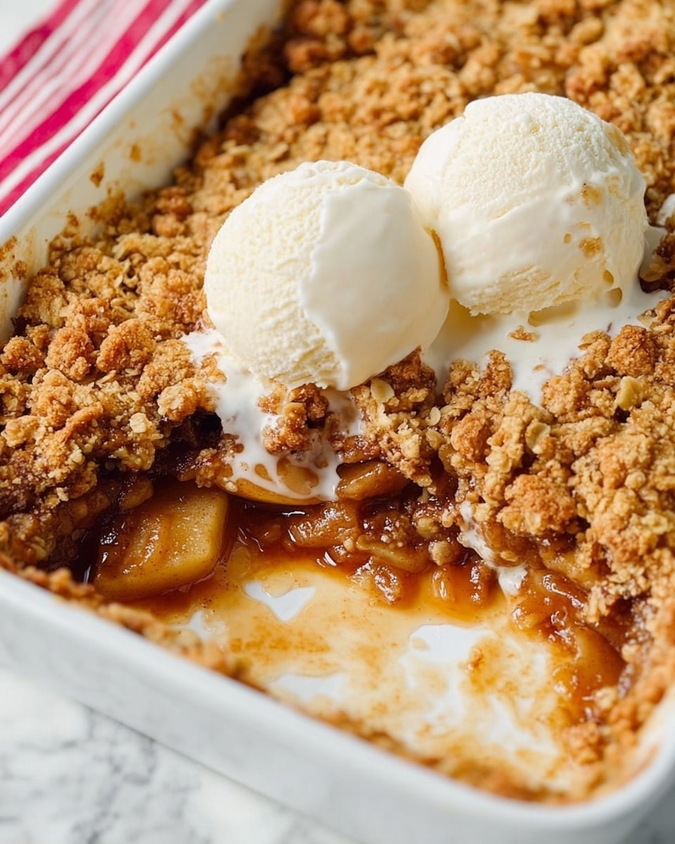 A close-up view of a white rectangular baking dish with a partially eaten apple crumble dessert inside. The dessert has three main layers: the bottom layer is soft cooked apple chunks in a shiny caramel sauce, the middle layer shows sticky juices mixing into the white dish, and the top layer is a thick, crumbly golden-brown crust with a rough, uneven texture. On top of the crumble, there are two round scoops of smooth, slightly melting vanilla ice cream, with soft drips running down the sides onto the crust. The baking dish sits on a white marbled surface with a faint red-striped cloth partially visible on the left side. photo taken with an iphone --ar 4:5 --v 7