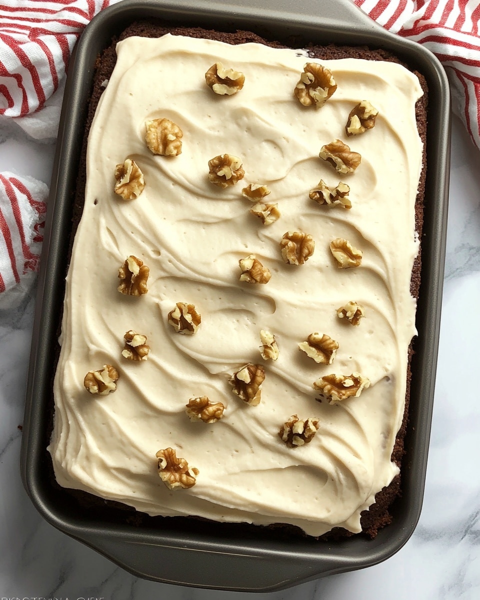 The image shows a rectangular cake in a dark metal pan with two main layers. The bottom layer is a dark brown cake, and on top is a thick, smooth layer of creamy white frosting with soft wave patterns. Roughly chopped light brown walnuts are scattered evenly across the frosting, adding texture and a crunchy look. The pan rests on a white marbled surface with a red and white striped cloth nearby. Photo taken with an iphone --ar 4:5 --v 6.1