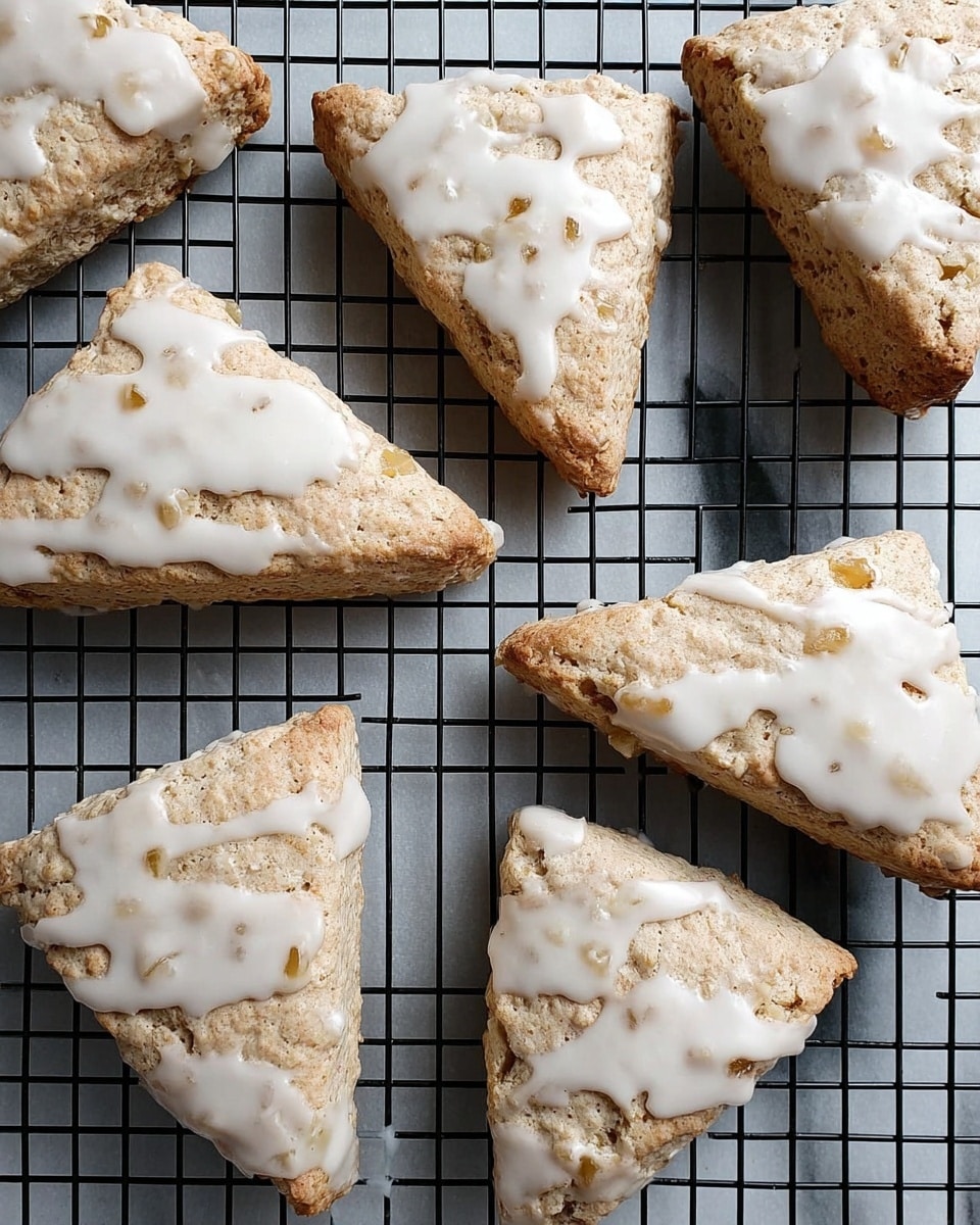 The image shows a close-up of a plate full of triangular scones stacked on top of each other. Each scone has a golden-brown crispy texture with visible bits of apple inside. A light drizzle of white icing covers the top of each scone, adding a shiny contrast to the warm baked color. The scones are arranged on a white plate, sitting on a white marbled surface. Photo taken with an iphone --ar 4:5 --v 7