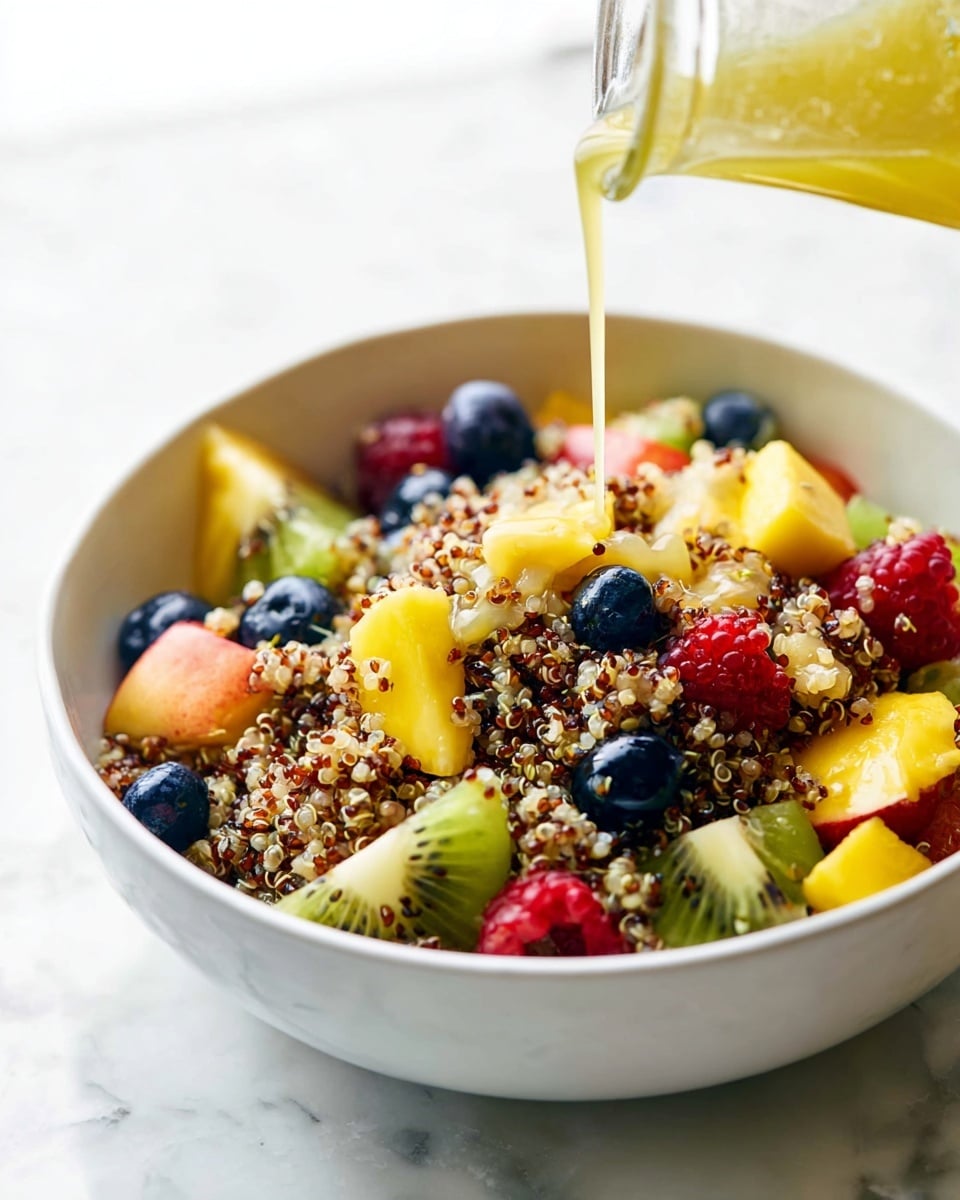 A white bowl filled with a colorful mix of quinoa and fresh fruit sits on a white marbled surface; the quinoa forms the base layer with its small, round grains in light tan and dark brown colors, while on top sits a variety of fruit pieces including bright yellow mango chunks, green kiwi slices, dark blue blueberries, red raspberries, and orange segments. A light yellow liquid is being poured from a clear glass bottle onto the quinoa and fruit mix, creating a shiny coating over the top. The scene is bright and fresh, focusing on the textures and colors of the healthy ingredients. Photo taken with an iphone --ar 4:5 --v 7