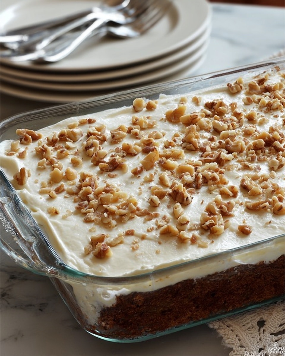 A rectangular clear glass dish holds a dessert with two visible layers: the bottom layer is dark brown and looks dense and moist, while the top layer is a smooth, creamy white frosting spread evenly across the surface. The frosting is sprinkled generously with chopped walnuts that vary in color from light to medium brown, adding texture on top. The dish is placed on a white marbled surface, and in the background, there are stacked white plates with silver forks resting on them. photo taken with an iphone --ar 4:5 --v 7