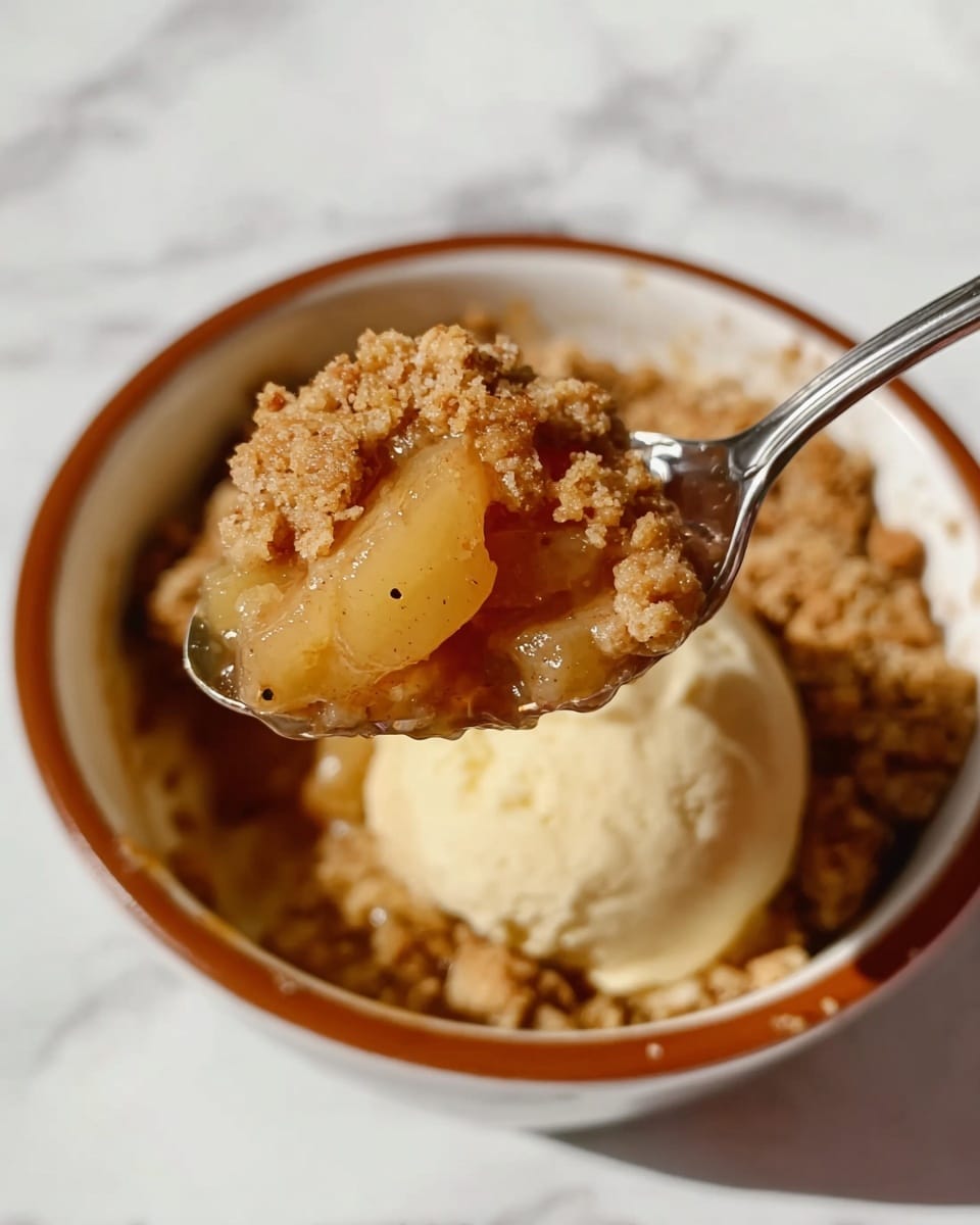 A round terracotta bowl filled with a warm crumble dessert, showing three main layers: a base layer of soft apples with some pieces visible, a thick, crumbly golden-brown streusel topping covering most of the fruit, and a melting scoop of creamy, pale vanilla ice cream sitting on top. The ice cream is slightly melting around the edges, blending softly into the warm crumble. A golden spoon rests inside the bowl, slightly dipping into the dessert. The bowl sits on a white marbled surface. Photo taken with an iphone --ar 4:5 --v 7