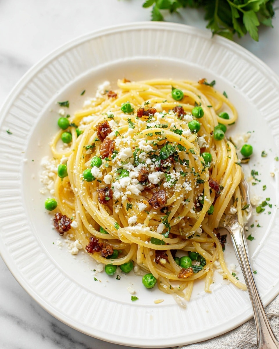 A white plate with ridged edges holds a small nest of light yellow spaghetti piled in the center. Scattered through the pasta are bright green peas and small crispy brown meat pieces. The spaghetti is sprinkled on top with crumbled white cheese and finely chopped green herbs. A fork rests partially wrapped in the spaghetti on the right side of the plate. The plate sits on a white marbled surface with a blurry green garnish in the top background. photo taken with an iphone --ar 4:5 --v 7