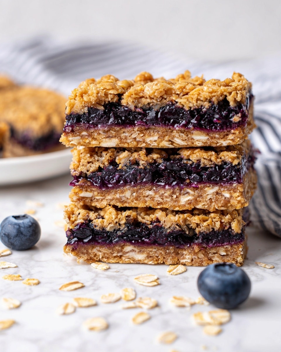 The image shows a stack of three oatmeal and blueberry bars placed on a white marbled surface. Each bar has three clear layers: the top and bottom layers are golden-brown oatmeal with a rough texture of oats, and the middle layer is a thick, dark purple blueberry filling with visible small seeds. The bars have a dense, crumbly look, with a few loose oats scattered around on the surface, along with two whole blueberries in the foreground. The background is softly blurred, showing a hint of a white plate and a striped cloth, all against the white marbled texture. photo taken with an iphone --ar 4:5 --v 7