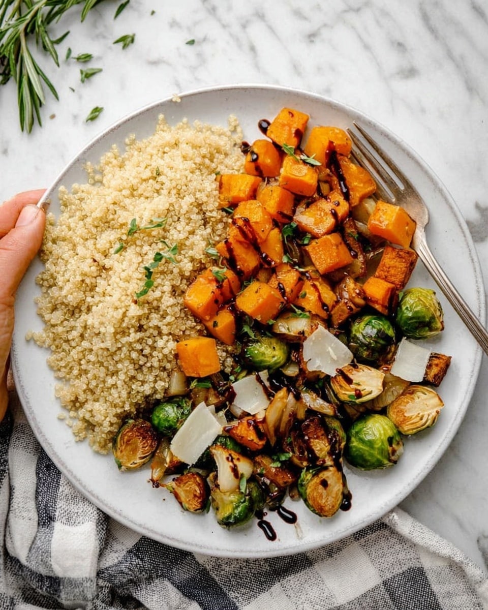 A white round plate is filled with two main sections: on the left side, there is a mound of light beige quinoa with a fluffy texture, topped with some small green herbs. On the right side, there is a colorful mix of roasted vegetables including bright orange cubes of butternut squash, halved green Brussels sprouts with browned edges, and small pieces of roasted onions in off-white shades. Thin flakes of white cheese and fresh green sprigs of rosemary are scattered on top, along with a drizzle of dark balsamic glaze creating lines across the vegetables. A silver fork rests on the upper edge of the plate. The plate sits on a white marbled surface with a gray and white checked cloth nearby. A woman's hand is not visible in the scene. photo taken with an iphone --ar 4:5 --v 7