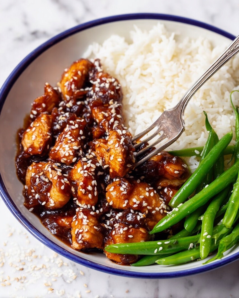 A white plate holds three sections of food on a white marbled surface: a mound of fluffy white rice on the left, bright green cooked green beans with a shiny texture on the right, and a pile of small, glossy brown chicken pieces coated in a thick sauce sprinkled with white sesame seeds at the bottom. Halved lime pieces are placed nearby on the top right, and a silver fork is seen on the lower right side. photo taken with an iphone --ar 4:5 --v 7