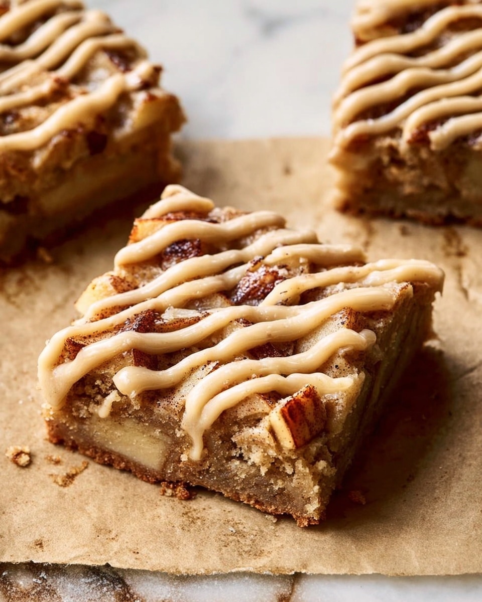 The image shows sixteen rectangular bars arranged on parchment paper over a wooden surface. Each bar has a base layer of light brown cake mixed with chunks of darker fruit or nuts inside. The top layer has a thick drizzle of creamy beige icing spread unevenly across each bar. To the top left of the bars, there is a white marbled surface holding a white cup with a red rim filled with a light brown drink, garnished with a cinnamon stick and star anise floating on top, adding a warm, cozy feel. A woman's hand is holding one of the bars near the top left corner. Some cinnamon sticks rest in the background on the wooden surface. The scene is warm and rustic, emphasizing textures and rich browns with light icing contrast. Photo taken with an iphone --ar 4:5 --v 7