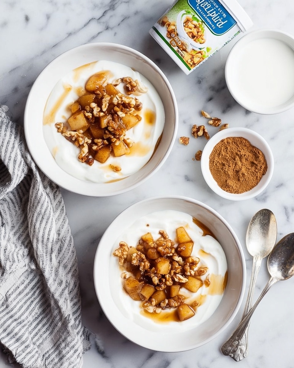 A white bowl filled with thick white yogurt as the base layer, topped with a mixture of cooked apple pieces in shades of light brown and golden yellow, mixed with small golden raisins and chopped walnut pieces spread unevenly over the fruit. The cooked fruit looks soft and coated with a light brown cinnamon sauce that spreads slightly over the yogurt, creating a warm contrast. A metal spoon is placed inside the bowl, resting in the yogurt. The bowl is set on a white marbled surface. photo taken with an iphone --ar 4:5 --v 7
