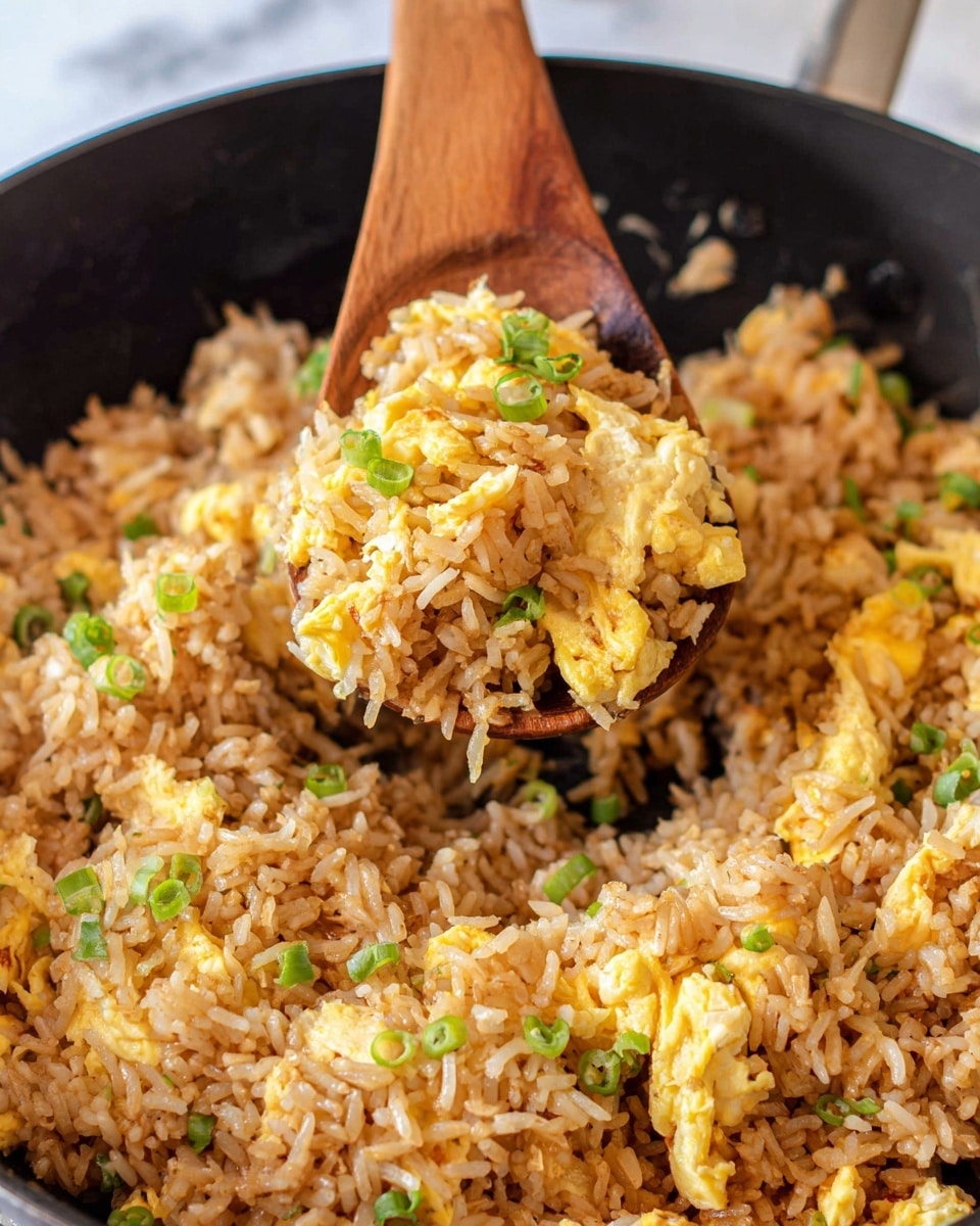 A red bowl filled with fried rice, showing long grains of rice mixed with scrambled egg pieces and green herbs scattered on top. The rice is light brown with some darker spots, giving it a cooked, soft texture. The bowl sits on a light tan woven mat, resting on a white marbled surface. To the right, a small white bowl holds dark red chili sauce with oil, and a pair of wooden chopsticks with floral patterns lies nearby. In the top edge of the image, part of another white bowl with rice and a small green herbs leaf are visible. Photo taken with an iphone --ar 4:5 --v 7