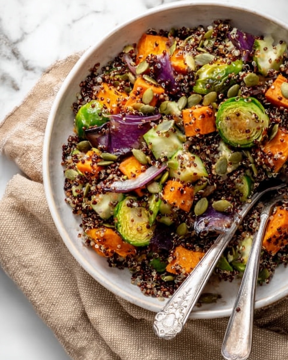 A clear glass bowl filled with a colorful fall quinoa salad showing several layers: the bottom layer contains dark red quinoa grains, mixed with bright green spinach leaves and light green cucumber pieces scattered throughout; on top are thick chunks of orange roasted sweet potatoes and pieces of purple cabbage adding contrasting color; the salad is mixed with small green Brussels sprouts halves and some carrot strips. The bowl sits on a white marbled surface with a white cloth napkin nearby, and the edge of a glass jar with yellow dressing is visible at the side. A red lid with a white label that says