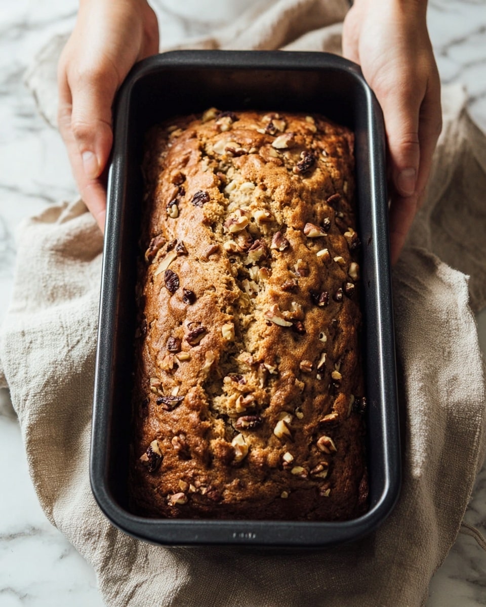A loaf of banana bread with a golden brown crust sits on white parchment paper over a wooden board. The top is studded with chopped nuts and drizzled with white icing that runs down the sides in thick lines. A ripe yellow banana is blurred in the background on a white marbled surface. photo taken with an iphone --ar 4:5 --v 7