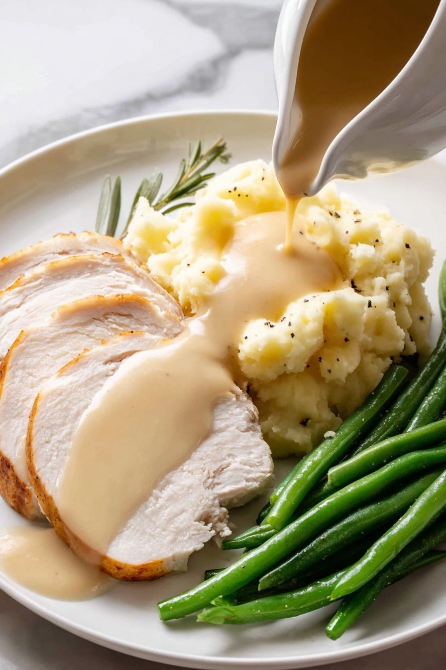 A white gravy boat filled with light brown smooth sauce, speckled with black pepper, sits on a round white speckled plate with a brown rim. Two fresh green herb sprigs, one rosemary and one sage leaf, rest beside the gravy boat on the plate. A shiny silver spoon lies on the plate next to the gravy boat, and the entire setting is placed on a white marbled surface. photo taken with an iphone --ar 2:3 --v 7 - Easy Turkey Gravy from Drippings, homemade turkey gravy, turkey drippings gravy, simple turkey gravy recipe, best turkey gravy