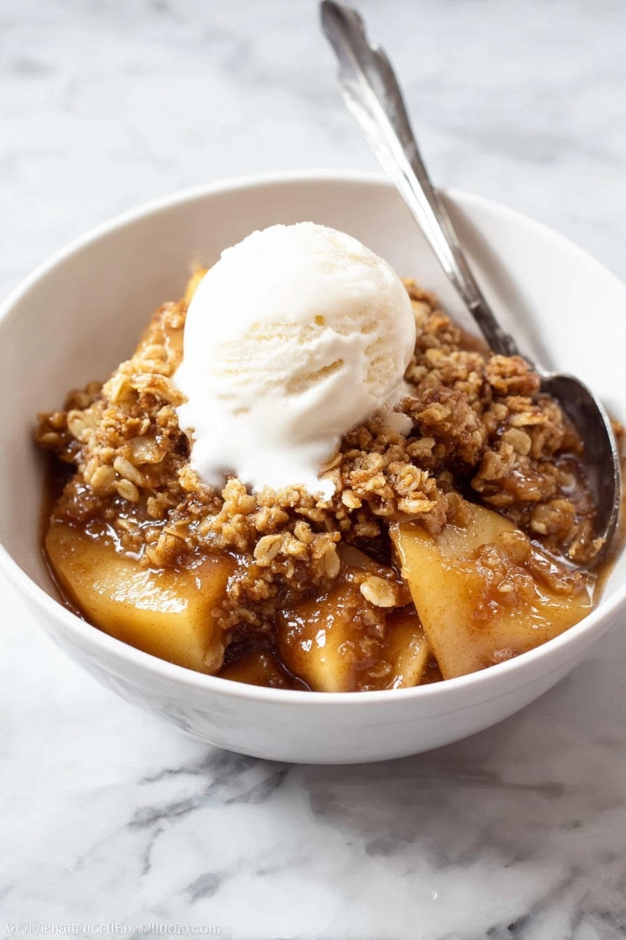 The image shows a white oval dish filled with a warm, brown dessert that has two main layers. The bottom layer is soft, cooked apple slices with a shiny, caramel-like sauce that looks sticky and rich. The top layer is a crumbly, golden brown oat and nut topping that covers the apples in uneven chunks. A silver spoon is dipped into the right side of the dish, slightly disturbing the topping and revealing more of the apple filling underneath. The dish is placed on a white marbled surface, making the warm colors of the dessert stand out. photo taken with an iphone --ar 2:3 --v 7 - Apple Crisp, Best Apple Crisp, Easy Apple Crisp, Homemade Apple Dessert, Cinnamon Apple Crisp