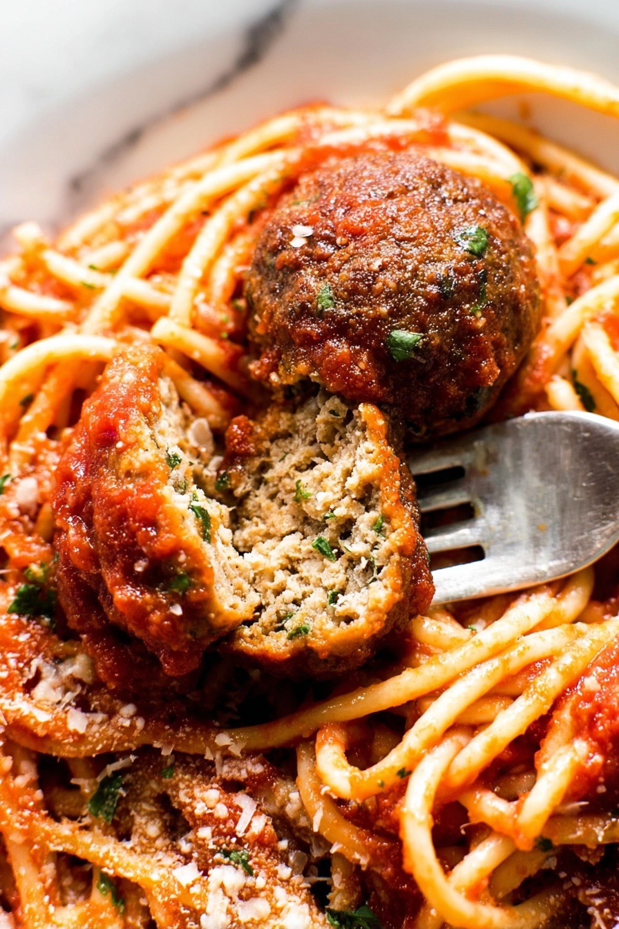 The image shows a close-up of a plate of spaghetti with tomato sauce and two meatballs, one whole and one cut in half to show its inside texture. The spaghetti is light orange with a smooth surface, coated with thick red tomato sauce that has small bits of herbs. The meatballs are brown with a slightly rough texture, and the cut meatball reveals a dense inside with green herbs mixed in. There is a sprinkling of grated cheese and chopped green herbs on top. A silver fork is placed under the cut meatball. The plate is white, and the background is a white marbled texture. photo taken with an iphone --ar 2:3 --v 7 - Classic Spaghetti and Meatballs, homemade spaghetti and meatballs, best spaghetti and meatballs, Italian spaghetti and meatballs, easy spaghetti and meatballs recipe