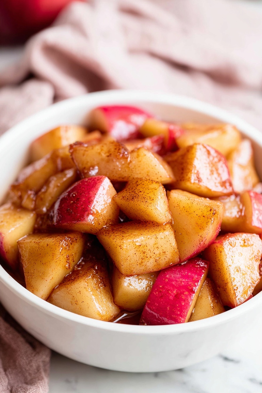 A black pan filled with evenly cooked, cubed apple pieces showing a mix of golden brown and red skin tones, lightly caramelized with a shiny texture scattered all over the pan; the pan handle is metal with visible wear and sits on a white marbled surface partially covered by a soft red and white checkered cloth. To the top right, two whole red apples rest on a small round wooden board. The image is bright and simple, focusing on the warm colors and textures of the cooked apples. photo taken with an iphone --ar 2:3 --v 7 - Easy Cinnamon Apples, cinnamon apples, easy apple dessert, fall apple recipes, quick fruit desserts