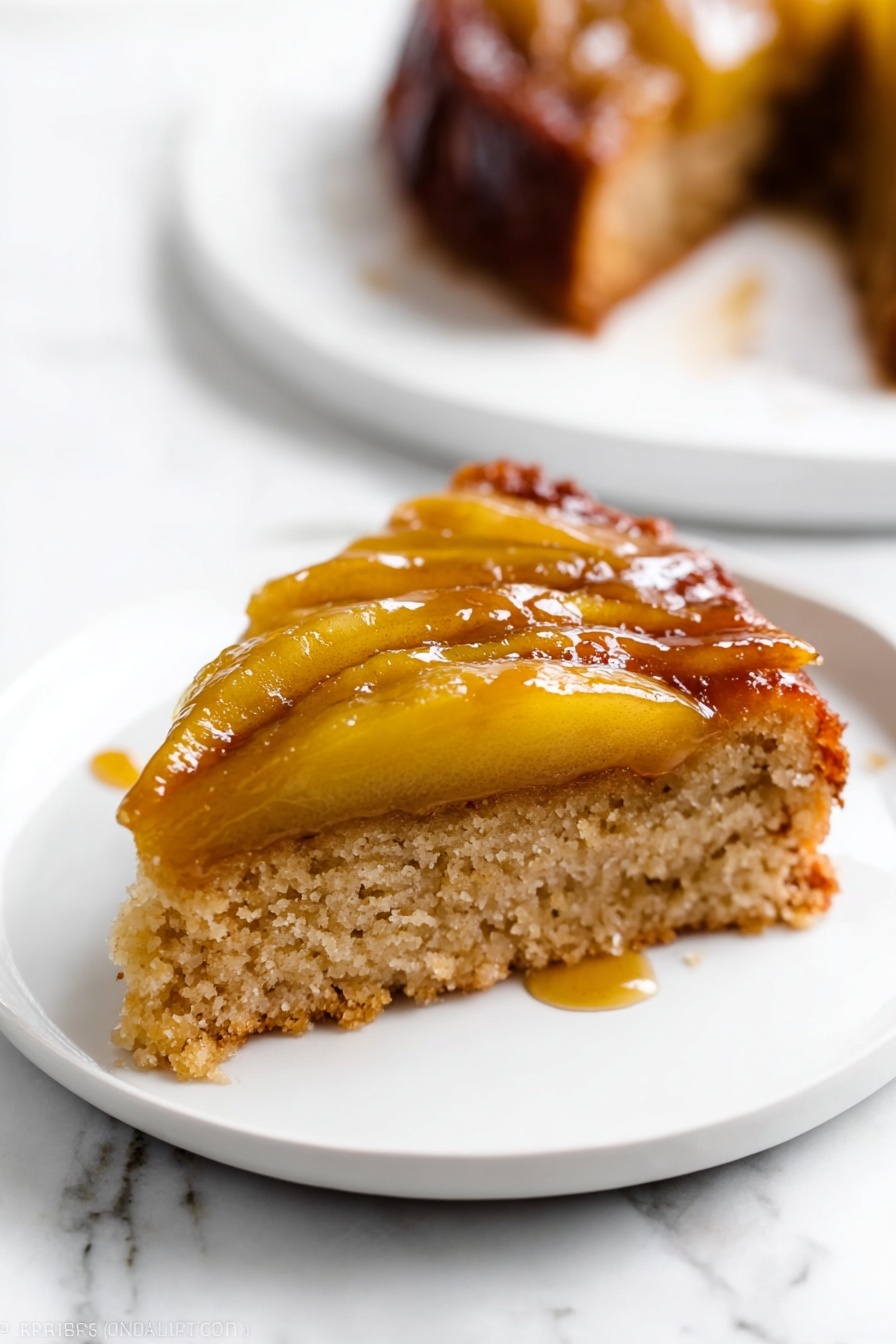A slice of cake with two layers is shown on a white plate set on a white marbled surface. The bottom layer is a light brown, soft, and spongy cake base. The top layer has cooked apple slices that are golden-yellow and shiny with caramel glaze, creating a sticky and glossy texture. The apple slices lie flat on the cake, and some syrup has slightly dripped onto the plate. In the background, there is a blurred white plate with another piece of the same cake. Photo taken with an iphone --ar 2:3 --v 7 - Caramel Apple Upside Down Cake, caramel apple dessert, fall apple cake, caramel upside down cake, homemade apple cake