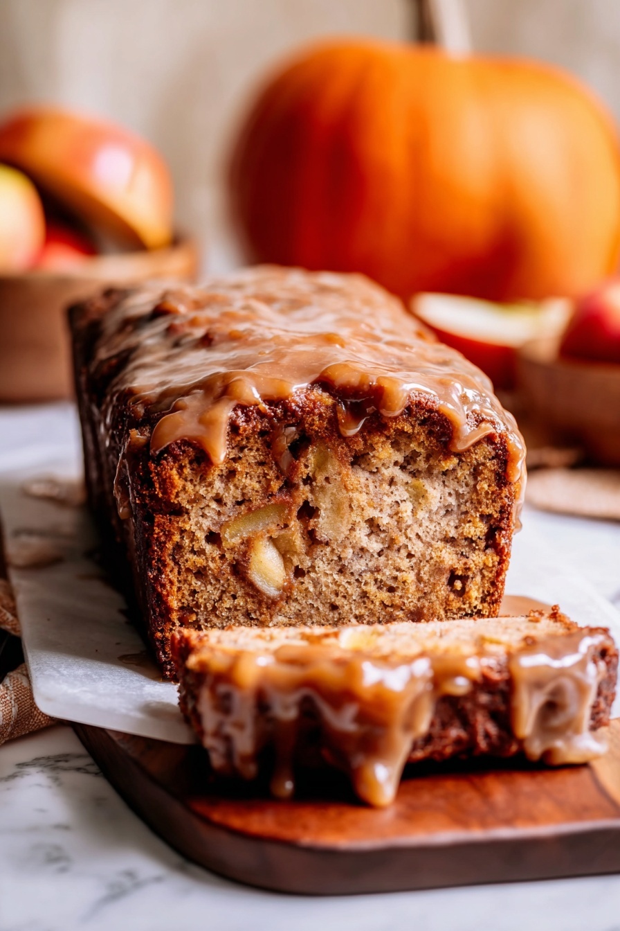 A loaf cake sits on a wooden board over a white marbled surface, sliced at the front showing its dense, light brown inside with visible chunks of apple. The top layer is a thick, sticky, darker brown glaze that drips down the sides, giving the cake a shiny look. In the background, there is a small orange pumpkin and a wooden bowl with apples that add warm tones to the image. The photo is warm and cozy, focusing tightly on the textures of the cake and glaze, with a soft, light blur in the background. photo taken with an iphone --ar 2:3 --v 7 - Amish Apple Fritter Bread, cinnamon apple bread, fall baked goods, apple bread with glaze, homemade apple bread recipe