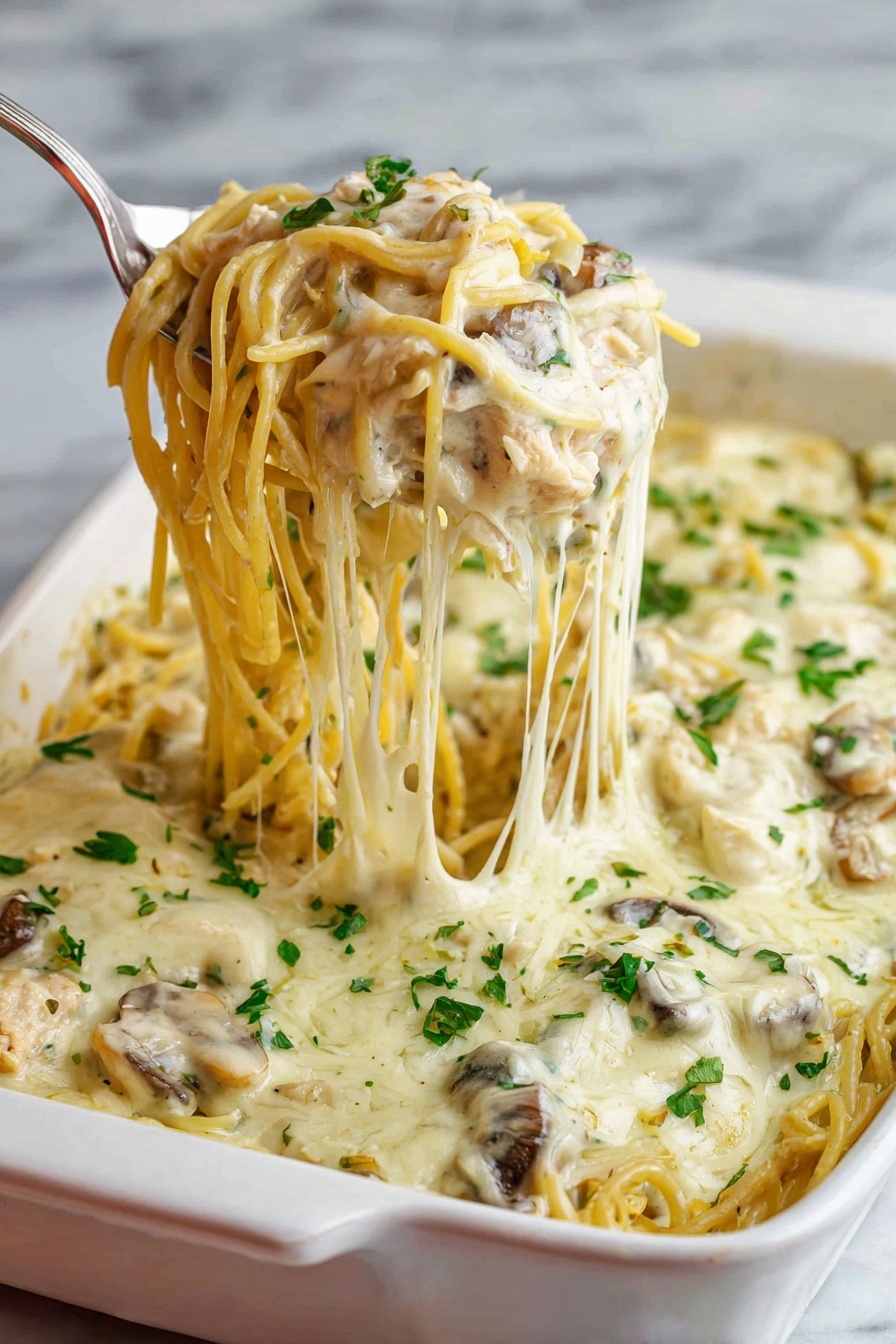 A white baking dish filled with creamy baked spaghetti is shown, featuring one thick layer of pasta mixed with mushrooms and shredded chicken, all covered with a smooth, melted white cheese sauce. The top layer is sprinkled with chopped fresh green herbs. A silver serving spoon lifts a portion of the spaghetti noodles, showing the soft texture and strands of melted cheese stretching from the dish. The background has a white marbled texture. Photo taken with an iphone --ar 2:3 --v 7 - Easy Chicken Tetrazzini Bake, chicken tetrazzini casserole, creamy chicken pasta bake, comforting chicken casserole, family-friendly dinner recipes