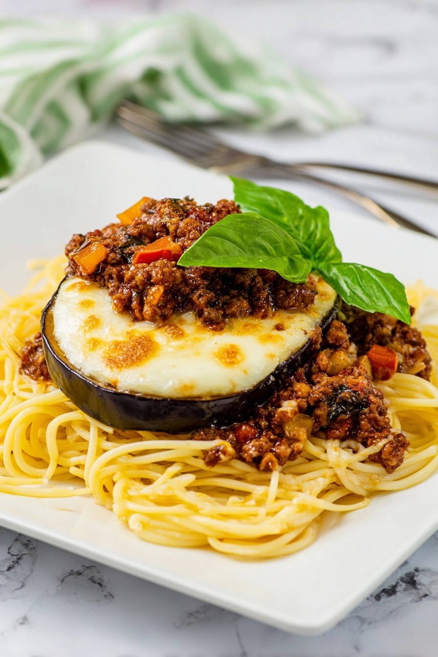 The dish shows a pile of yellow spaghetti noodles spread in a loose mound on a white square plate with rounded edges. On top of the noodles, there are slices of cooked eggplant with a glossy purple skin and soft interior, covered by a layer of melted, slightly browned white cheese. Between the eggplant layers, there are pieces of browned ground meat mixed with small bits of red tomatoes and mushrooms, adding texture and color. The top is garnished with fresh green basil leaves, adding a bright, leafy contrast. The plate sits on a white marbled surface with an orange and white striped cloth and a fork and knife placed behind it near the upper left edge. Photo taken with an iphone --ar 2:3 --v 7 - Eggplant Parmesan Spaghetti with Meat Sauce, gluten-free eggplant pasta, Italian comfort food recipes, easy eggplant spaghetti, hearty meat sauce dishes