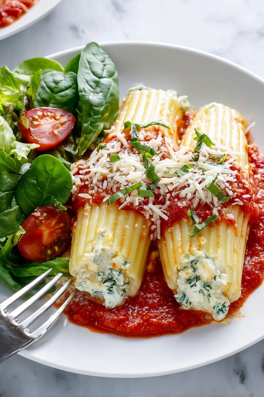 A white baking dish filled with seven folded pasta shells arranged in two rows. Each shell is stuffed with a white creamy filling and topped with bright red tomato sauce that is chunky and spread in small piles along the top. Fresh green basil leaves and small bits of grated white cheese are scattered on top, adding color contrast. The thick red sauce lines the bottom and sides of the dish, and the pasta shells have a ridged texture and a soft yellow color. The dish sits on a white marbled surface. Photo taken with an iphone --ar 2:3 --v 7 - Three Cheese Manicotti Bake, cheesy manicotti casserole, Italian baked pasta, cheesy manicotti recipe, family-friendly Italian dinner