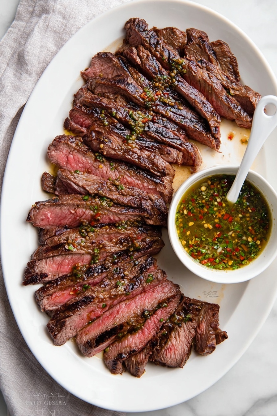 A white oval plate holds about twelve slices of grilled steak arranged in a slightly fanned out layer from left to right. The steak slices are medium-rare, showing a mix of deep brown outer edges with char marks and a pink-red center. To the right side of the plate, a small white bowl filled with a green sauce, flecked with red and yellow spices, sits partially on the plate with a white spoon inside it. The plate is set on a white marbled surface with a light gray cloth partially visible on the left side. Photo taken with an iphone --ar 2:3 --v 7 - Perfect Chimichurri Flank Steak, Chimichurri Flank Steak Recipe, Flank Steak with Chimichurri, Easy Chimichurri Steak, Grilled Flank Steak with Chimichurri