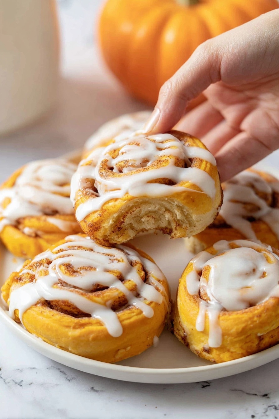 A white plate filled with six bright orange spiral rolls, each topped with a thick drizzle of white icing. The rolls have multiple visible layers with a soft, doughy texture and a cinnamon-spice swirl inside that adds a speckled light brown pattern. A woman's hand is gently lifting one roll from the plate, showing more of its smooth icing on the top center. The background is a white marbled texture with a small orange pumpkin blurred in the back. photo taken with an iphone --ar 2:3 --v 7 - Pumpkin Cinnamon Rolls with Cream Cheese Glaze, fall pumpkin cinnamon rolls, homemade pumpkin cinnamon rolls, easy pumpkin cinnamon roll recipe, pumpkin dessert ideas