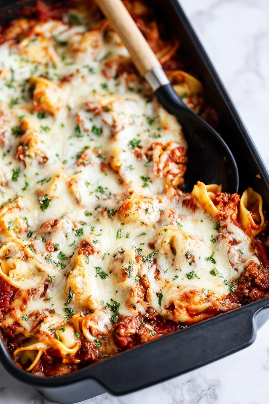 The image shows a large black baking dish filled with a layered pasta bake. The bottom layer has visible tomato sauce with small chunks of meat, rich red in color. On top of this is a thick layer of melted white cheese, which looks creamy and slightly browned in some spots. Scattered green herbs, probably parsley or basil, are sprinkled over the cheese, adding color contrast. There are curled pasta pieces, possibly tortellini, peeking through the cheese layer, coated in sauce and cheese. A black spoon with a wooden handle rests inside the dish near the top corner. The dish is placed on a white marbled surface. Photo taken with an iphone --ar 2:3 --v 7 - Baked Tortellini Casserole with Italian Cheese, creamy tortellini bake, cheesy Italian tortellini casserole, easy baked tortellini dishes, hearty cheesy pasta bake