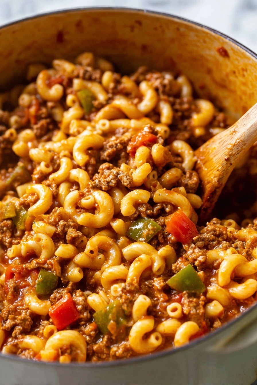 The image shows a close-up of a pot filled with elbow macaroni pasta mixed with ground meat, diced tomatoes, and chopped green bell peppers. The pasta is soft and coated with a rich reddish-brown sauce. The ground meat is crumbled small and evenly spread throughout the dish. Bright red tomato pieces and small chunks of green bell peppers add pops of color. A wooden spoon is stirring the mixture on the right side. The pot has a soft brown inside texture, and the background is a white marbled surface. photo taken with an iphone --ar 2:3 --v 7 - American Chop Suey, easy American Chop Suey, quick American Chop Suey, comforting American Chop Suey, one-pot American Chop Suey