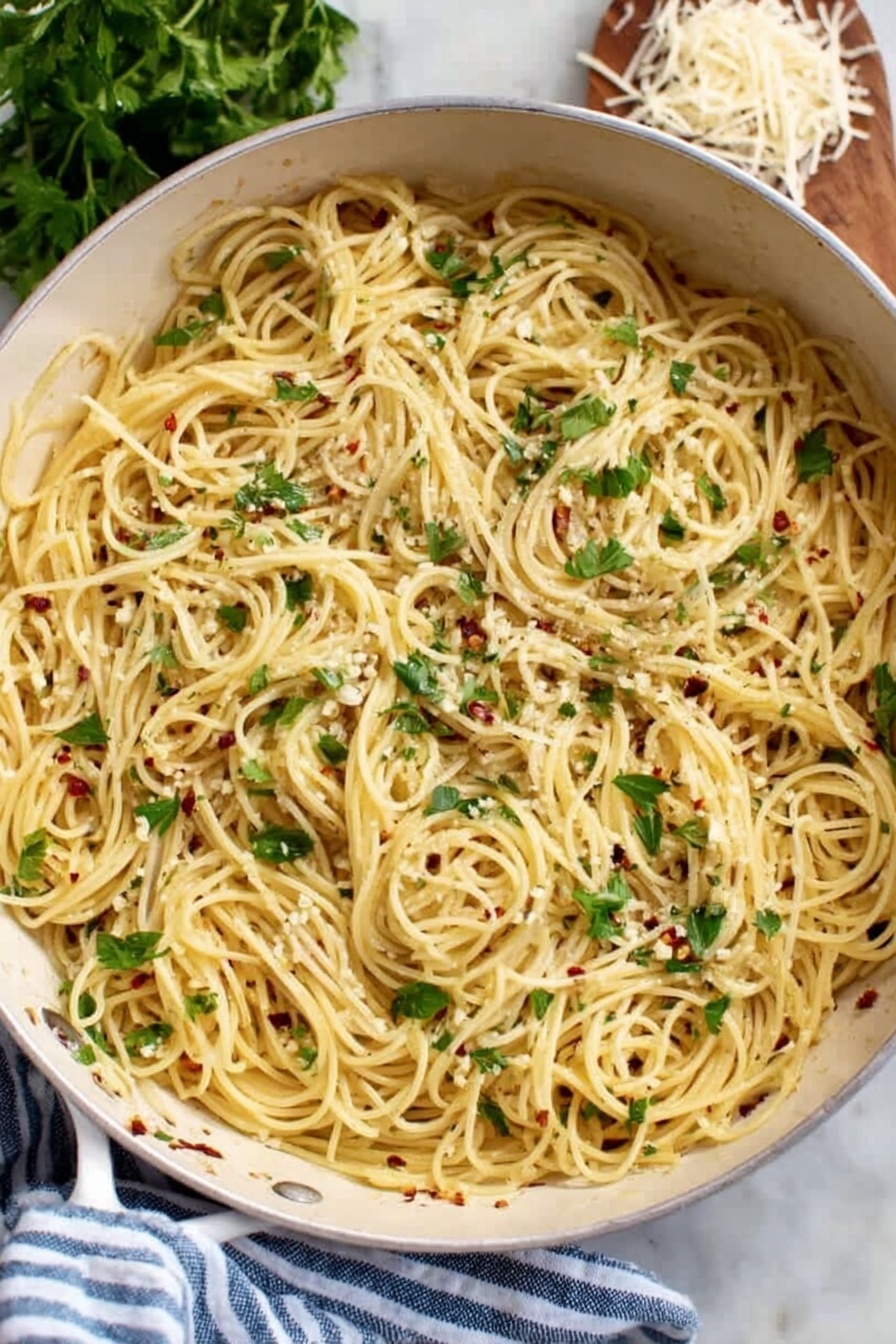 A white pan filled with a single layer of thin spaghetti pasta cooked and mixed with small bits of white garlic and red chili flakes spread throughout. Fresh green parsley leaves are scattered on top, adding a touch of color and freshness. The pan rests on a white marbled surface next to a blue and white striped cloth, with fresh parsley and some shredded cheese partially visible in the background. Photo taken with an iphone --ar 2:3 --v 7 - Garlic Infused Spaghetti Aglio e Olio, garlic pasta recipe, easy Italian pasta, quick garlic spaghetti, flavorful garlic pasta dish