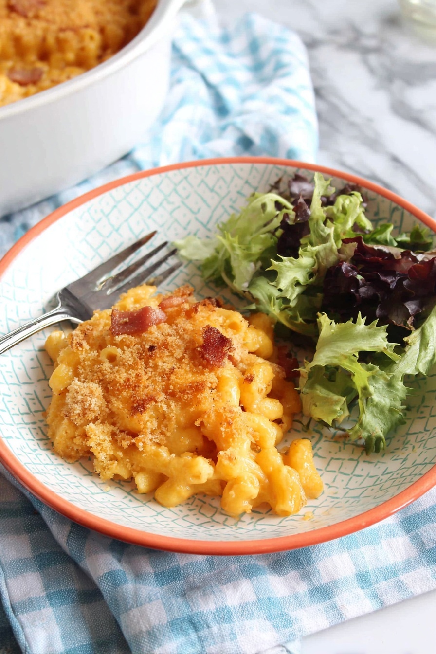 A white bowl with a light geometric pattern and orange rim holds a serving of baked macaroni and cheese topped with a golden breadcrumb crust with some browned spots. The macaroni pasta under the crust is creamy and orange, with small pieces of browned bacon or ham mixed inside. To the right side of the bowl is a small fresh salad of mixed green leaves, some dark purple and others bright green with curly texture. A silver fork rests on the left edge of the bowl. The bowl sits on a blue and white checkered cloth over a white marbled surface. In the bottom left corner, part of a white round baking dish filled with more macaroni and cheese is visible. photo taken with an iphone --ar 2:3 --v 7 - Chorizo Mac and Cheese, spicy cheesy pasta, smoky chorizo recipe, quick comfort food, creamy cheesy casserole