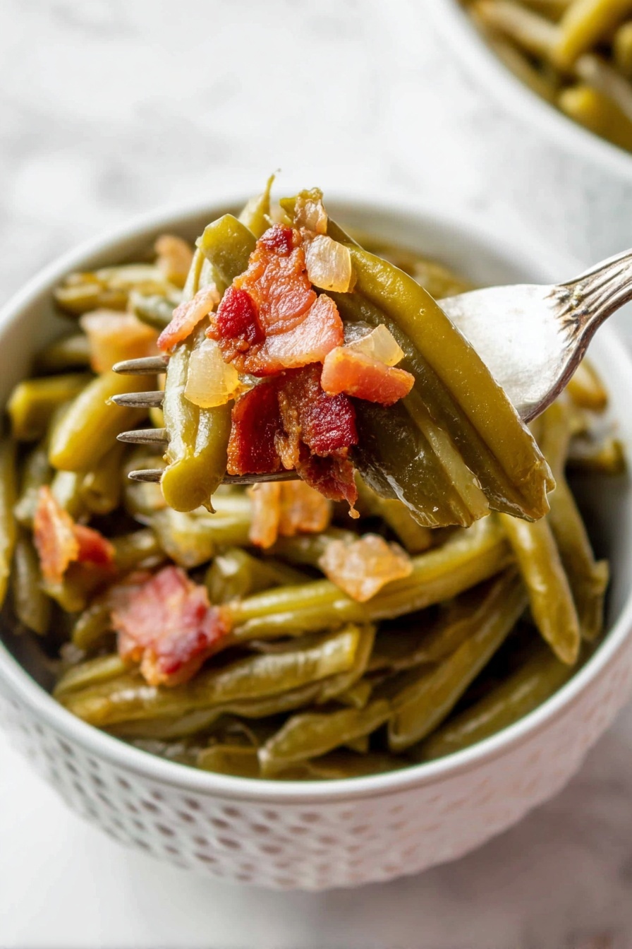 A white bowl with a pattern holds cooked green beans layered at the bottom, soft and shiny with a slightly wrinkled texture. On top, small chunky pieces of browned bacon with a reddish-brown tone and a bit of translucent cooked onion are mixed in. A fork lifts some green beans and bacon from the bowl, showing the layers clearly, with the vegetables still moist and the bacon crispy in places. The background is a white marbled surface. photo taken with an iphone --ar 2:3 --v 7 - Crock Pot Green Beans with Bacon, slow cooker green beans, bacon green bean side dish, easy green beans recipe, savory green beans with bacon